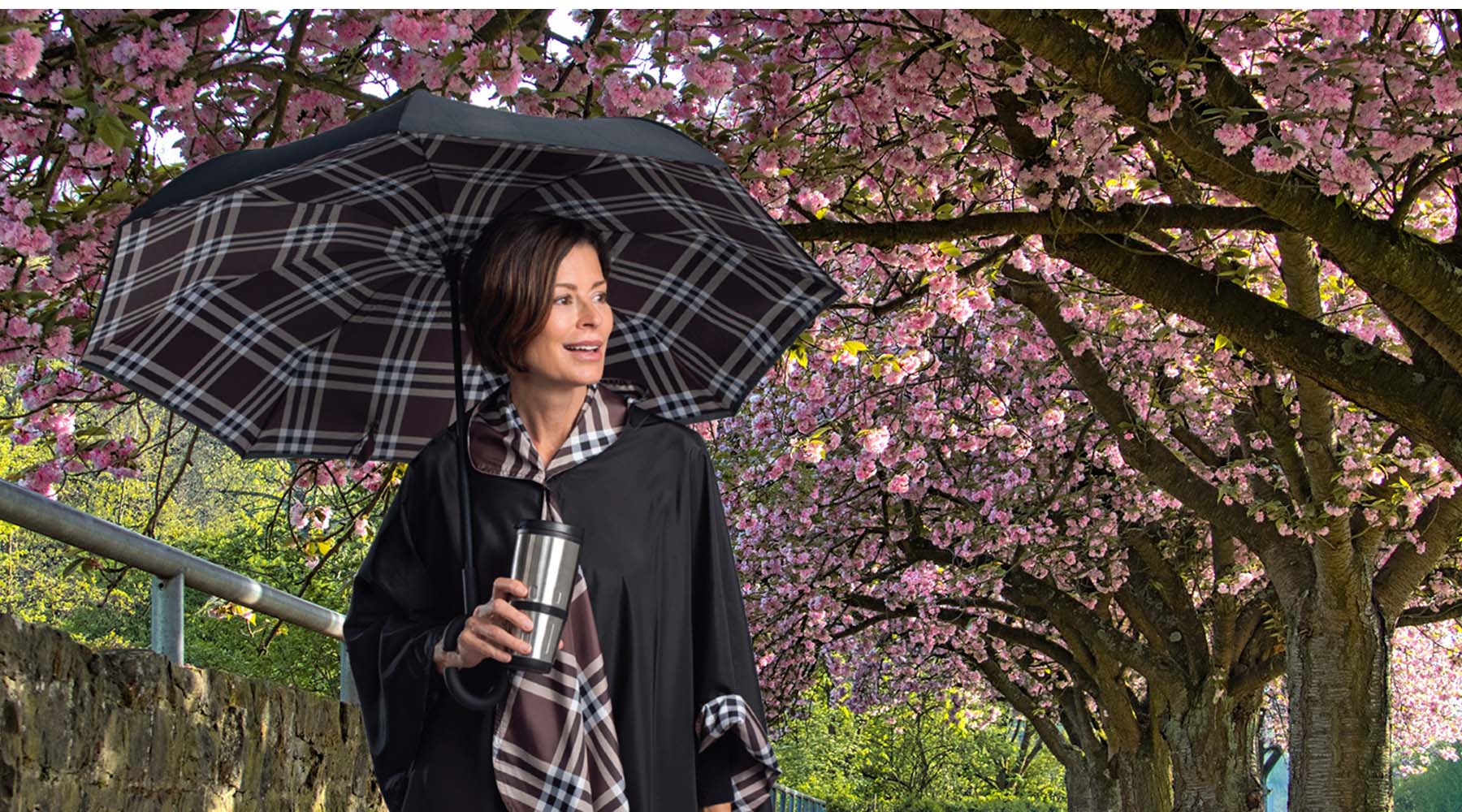 Coco plaid RainCaper and Coco Plaid reverse umbrella on a woman standing under a bloom of cherry trees